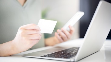 A person holding a phone and a card with his laptop in front of him