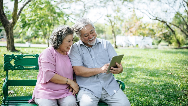 Two elderly couple looking at a tablet sitting on a bench
